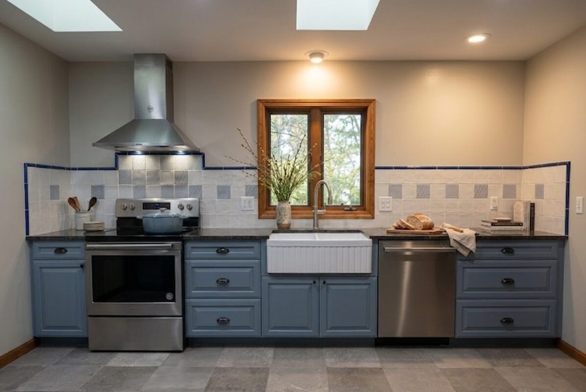 Full kitchen wall with slate blue cabinetry, black countertops, and a blue-tiled backsplash